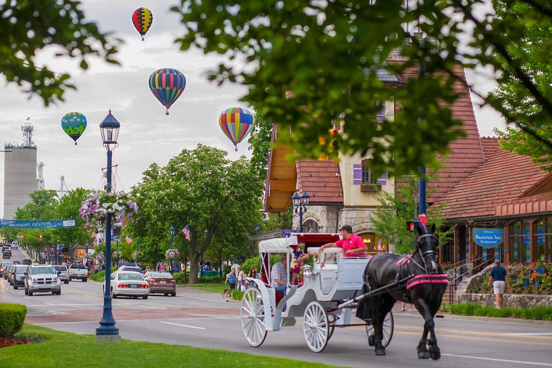 a horse drawn carriage on a street with hot air balloons in the background