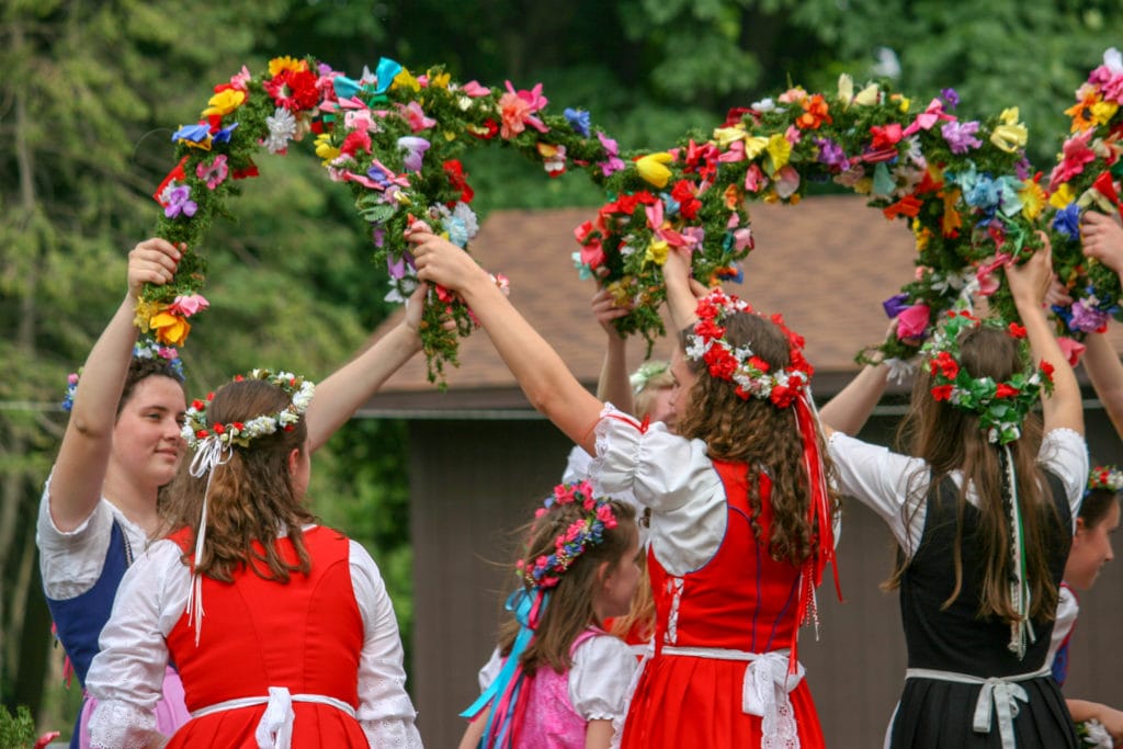young women wear festive dress and dance with rings of flowers