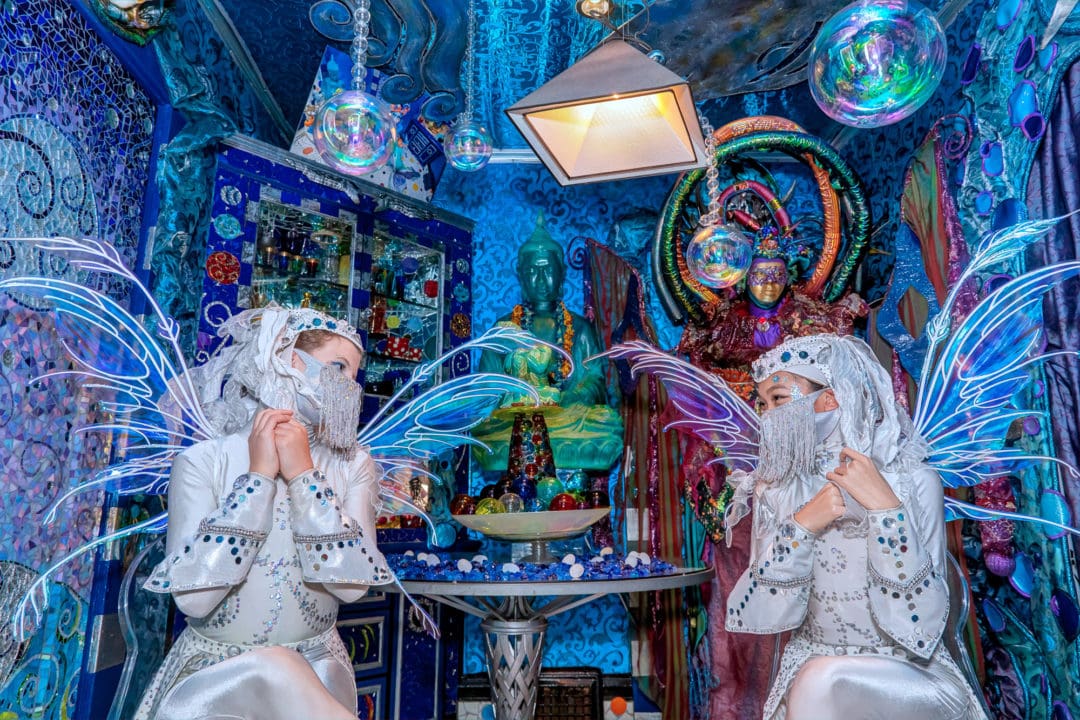 Two women dressed in white costumes with wings look at each other in a blue-tinted room