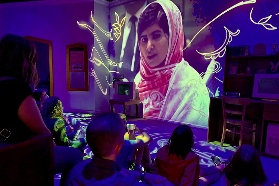 people watch a projection of malala in a dark room