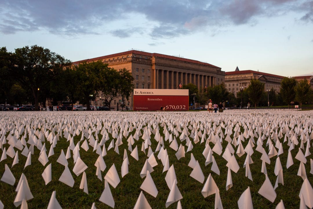 a sea of white flags with a sign displaying the words In America remember, 670,032
