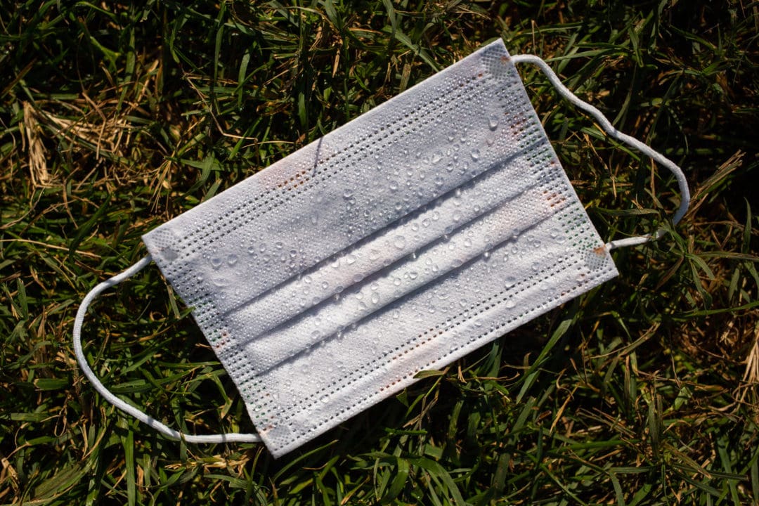 an unused surgical mask with dew drops on grass