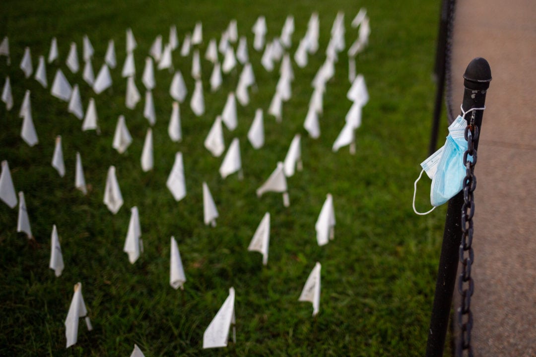 a blue surgical mask hangs on a pole near a field of white flags