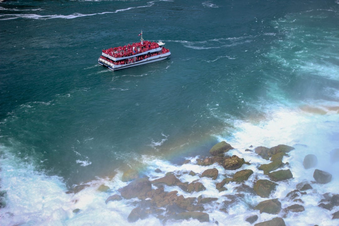 a boat floats at the base of niagara falls with a rainbow created out of the mist