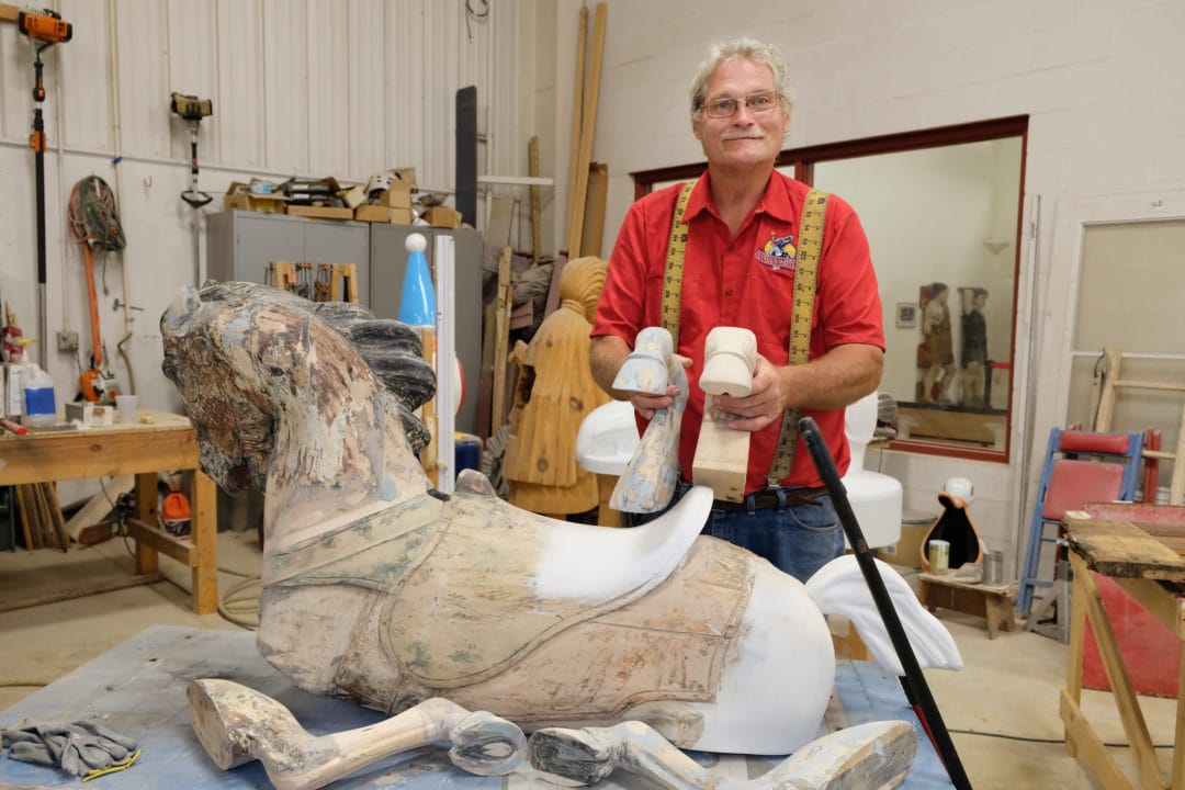 a man holds two carved wooden hooves in a workshop