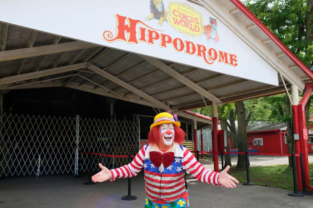 a clown in an american flag shirt stands in front of the entrance to the circus world hippodrome