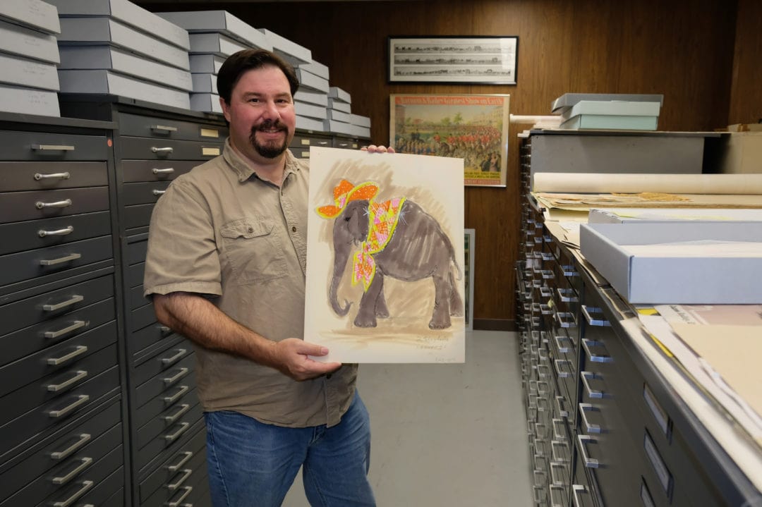 a man holds a sketch of an elephant wearing a cowboy hat and neckerchief