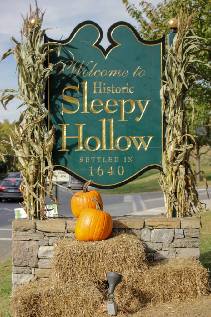 a sign says welcome to historic sleepy hollow with pumpkins, cornstalks, and hay bales
