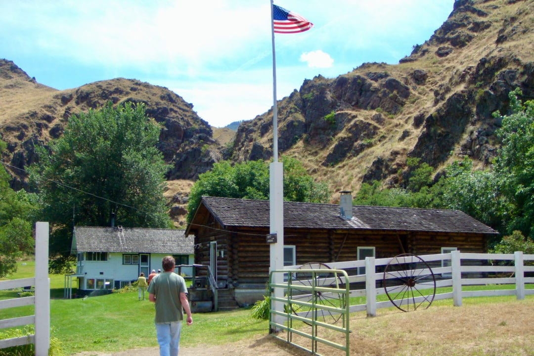a log cabin nestled in the mountains with a flag pole out front