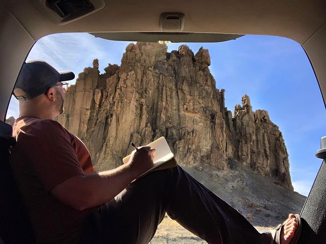 Man with a notebook looking up at a view of mountains