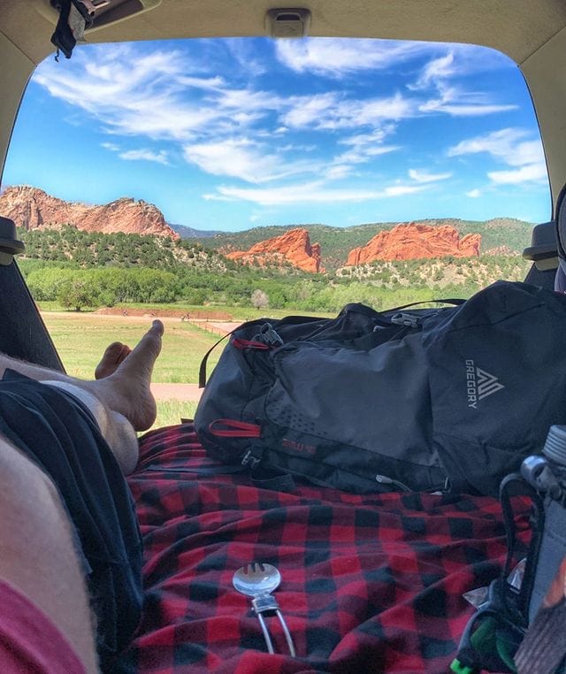 View from the back of a hatchback overlooking a green, red-rock view