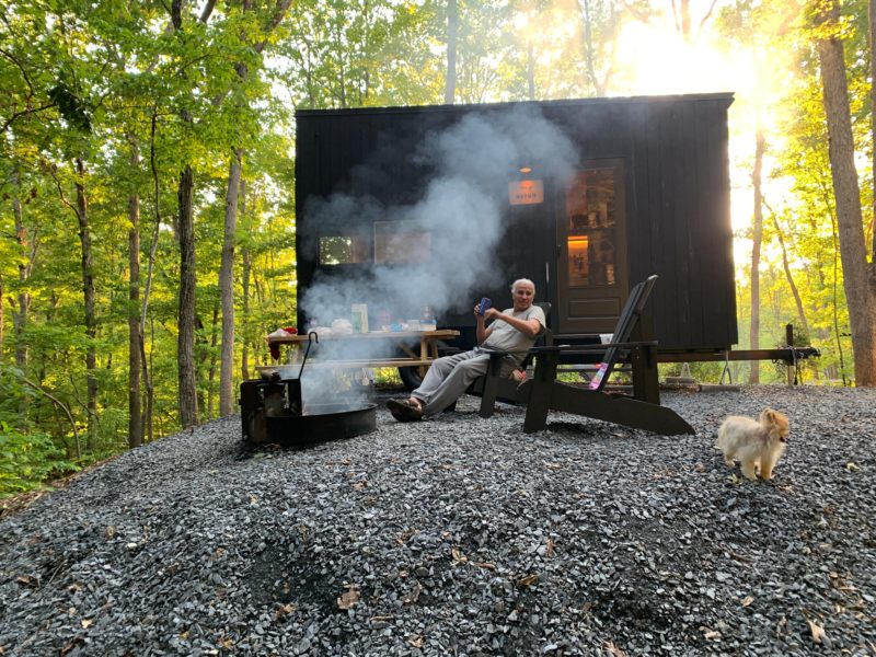 Man and tiny dog sitting near a campfire outside of the Getaway house.