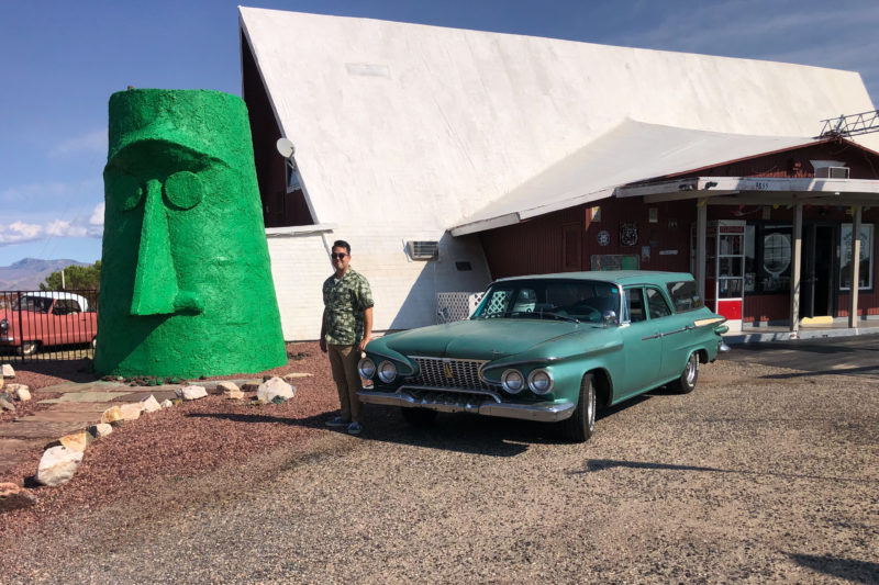 a green station wagon and man in front of a large green tiki head
