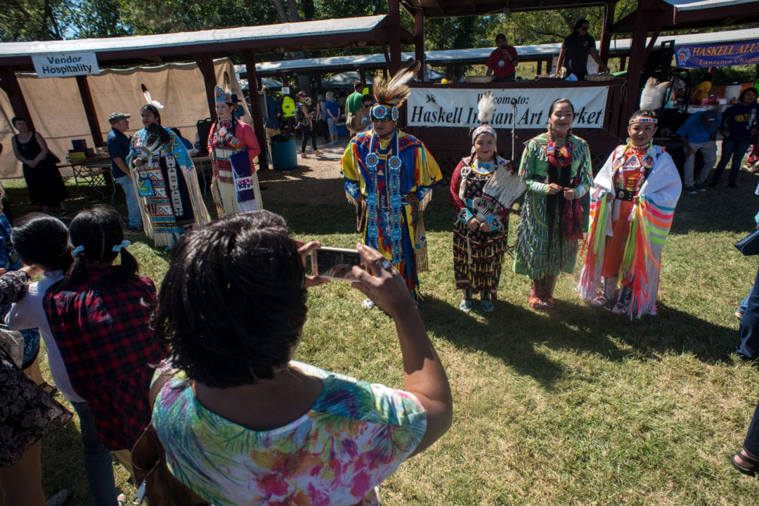 a woman takes a photo of a group of people in traditional native american dress