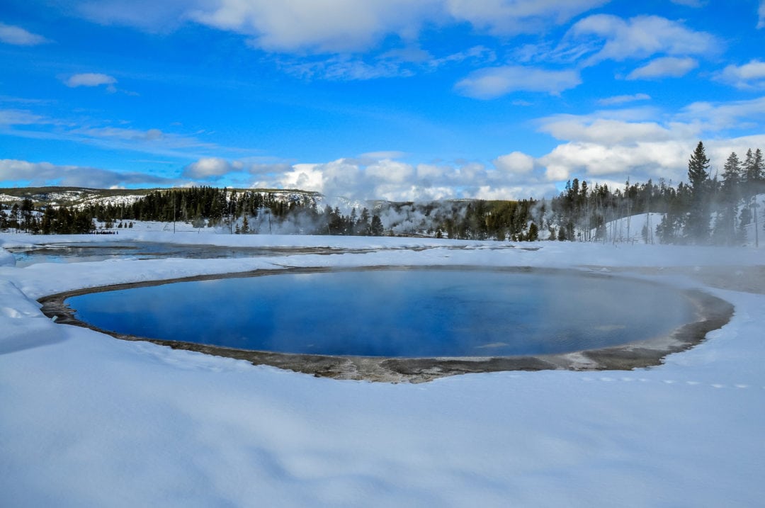 A geothermal pool sits at the center of a snowy landscape.