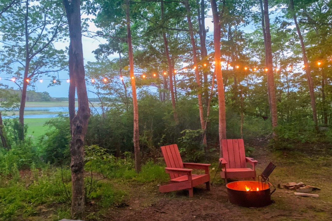 two red adirondack chairs sit next to a fire pit in the woods with string lights