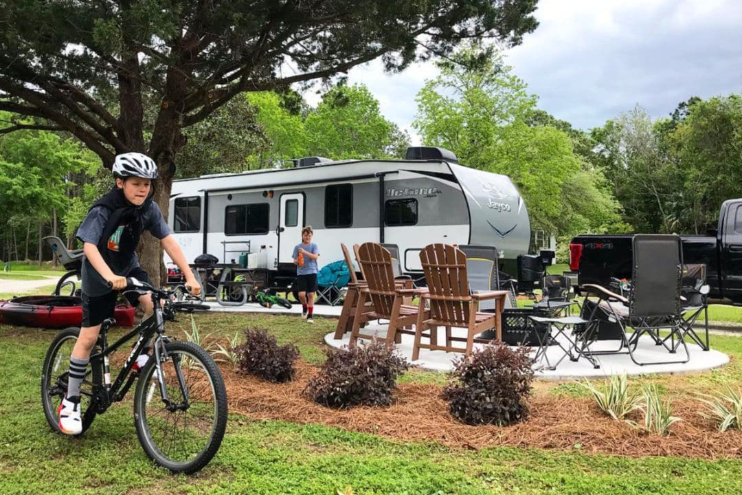 an RV parked at a campsite surrounded by chairs and a boy on a bike