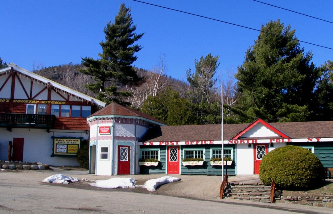 Exterior view of the North Pole post office, a green, red, and white building with some snow on the ground.