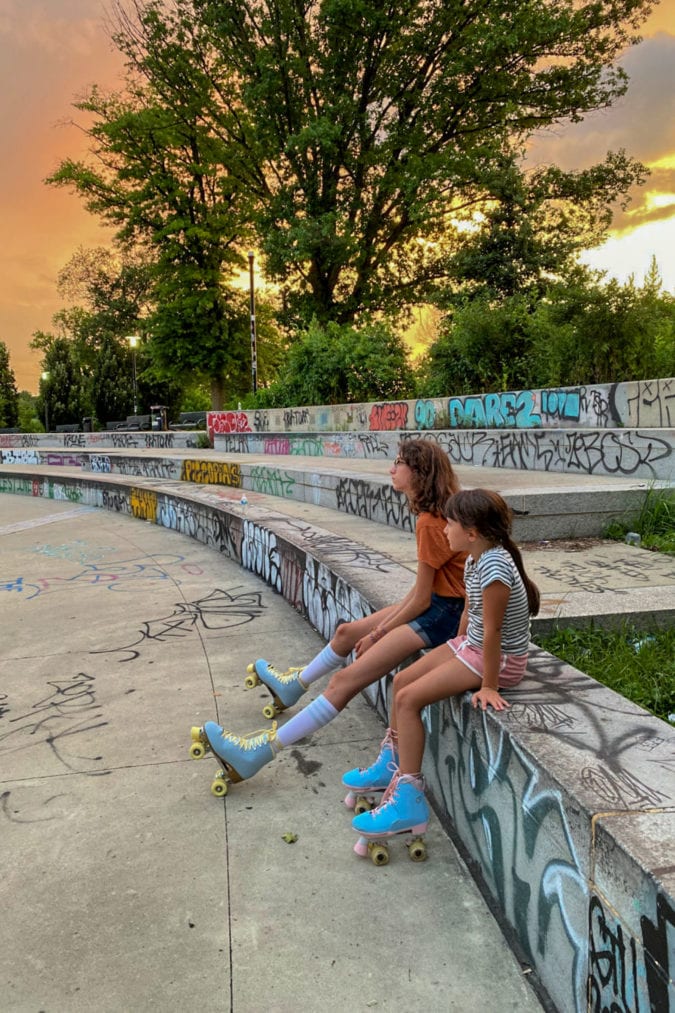 two people wearing shorts and rollerskates sit at a skate park covered in graffiti at sunset