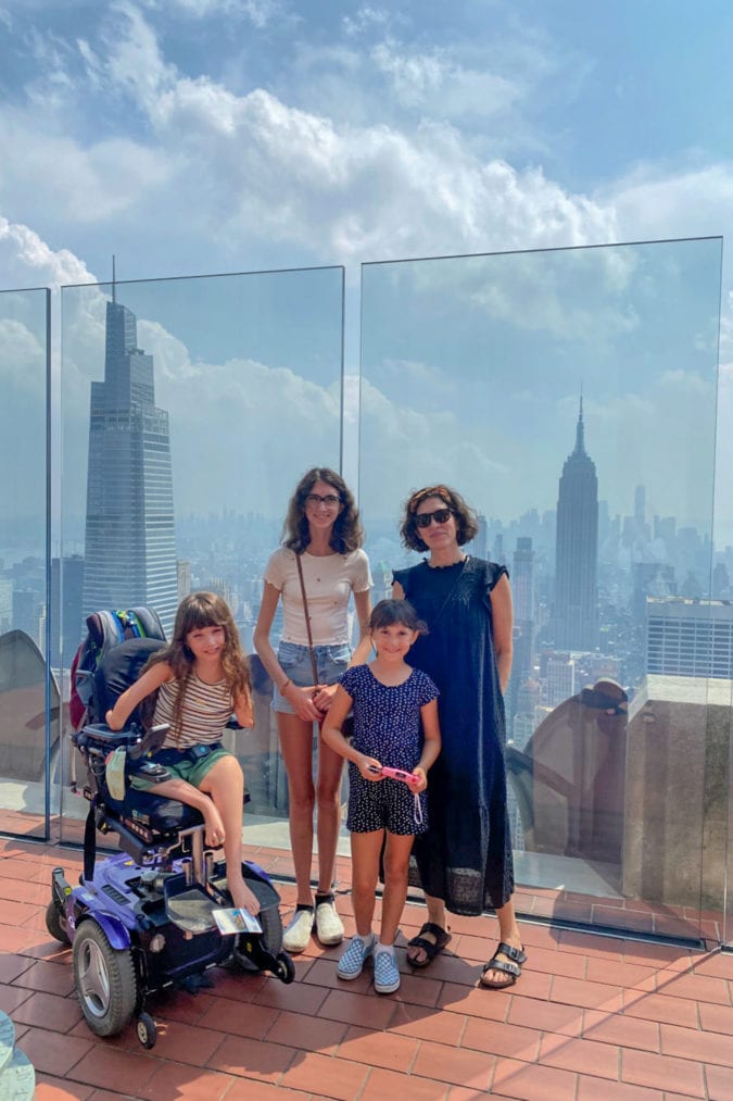 a family poses for a photo on the observation deck of rockefeller center with the empire state building in the background