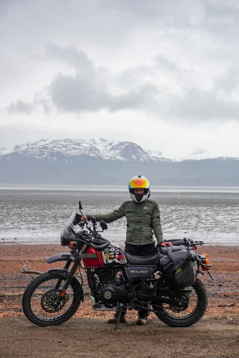 A woman standing on a beach with a motorcycle