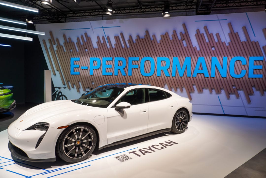 A white Porsche Taycan parked below giant letters that spell out "E-Performance"