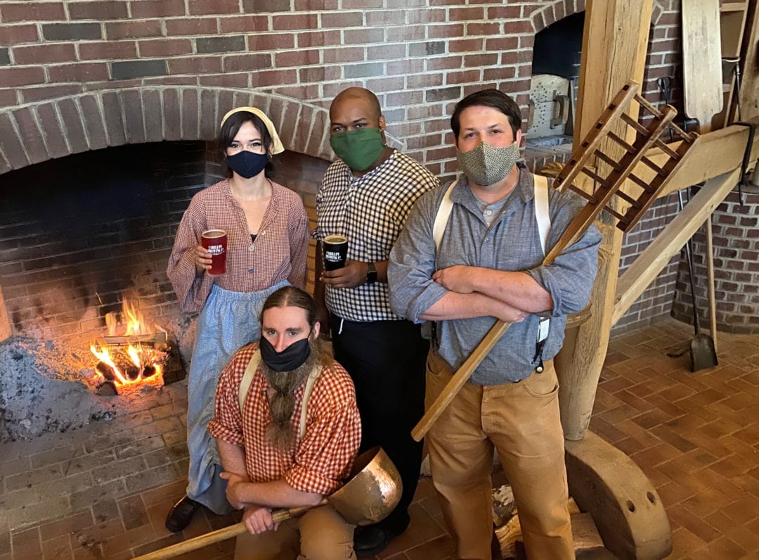 four people stand wearing face masks in front of a fire