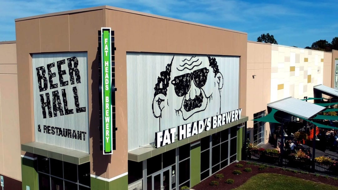 A tall building with a sign that reads "Fat Head's Brewery" and a big drawing of a mostly bald man in sunglasses and a mustache 