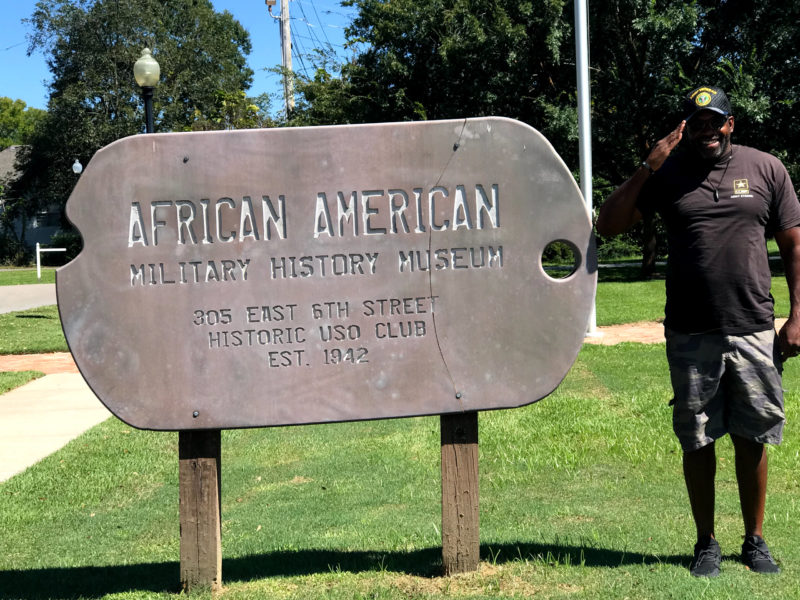 a man salutes next to a sign for the african american military history museum