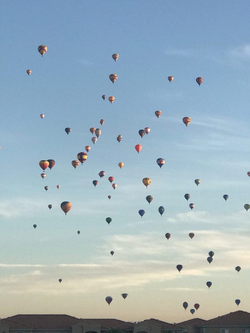 dozens of hot air balloons float above houses