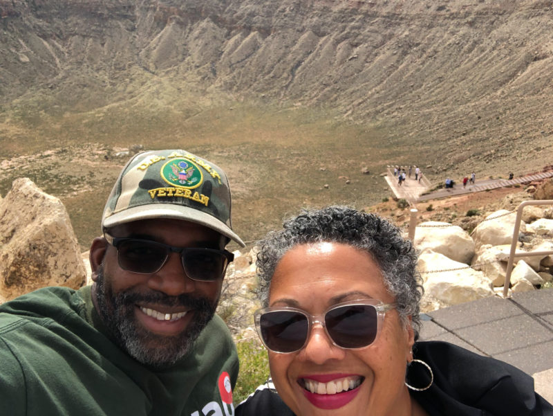 a couple poses in front of a large meteor crater