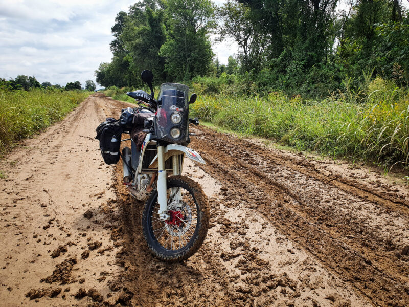Motorcycle parked in the middle of a muddy back road.