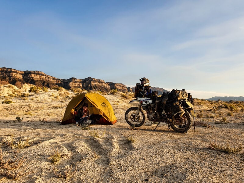 Woman camping in the desert with a tent and her motorcycle sitting nearby.
