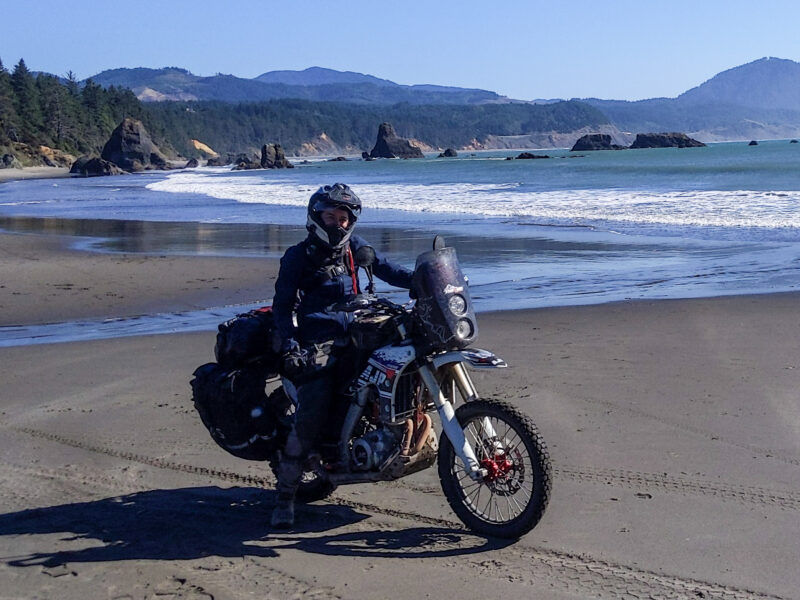 Woman riding a motorcycle along the beach in Oregon at Port Orford.