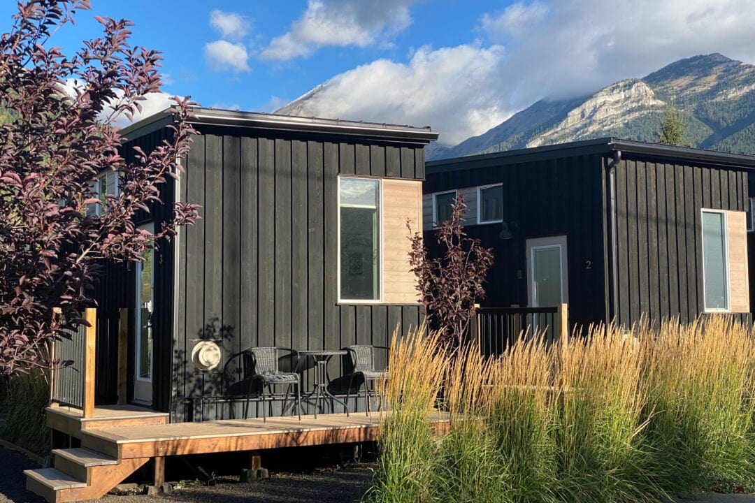 two tiny square wooden black homes with a porch set in the mountains