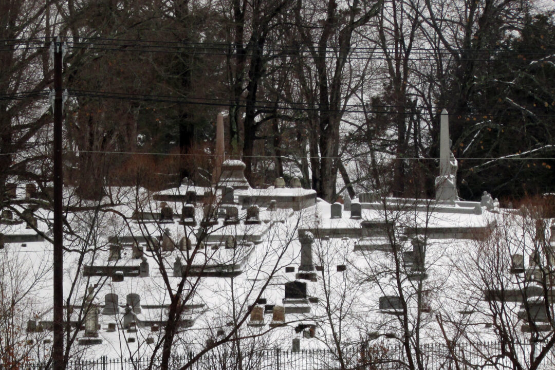 A hill in a cemetery with tombstones and layer of snow