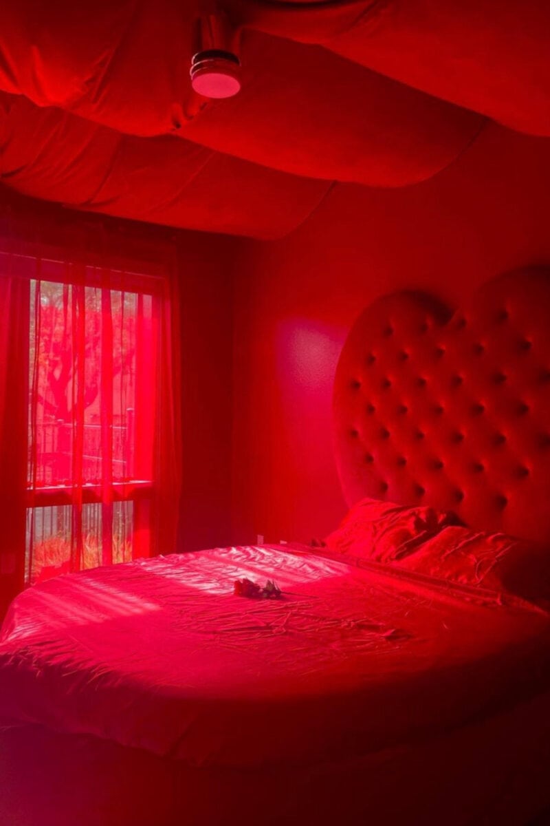 a red hotel room with red walls, ceilings, curtain and round bed with heart shaped headboard