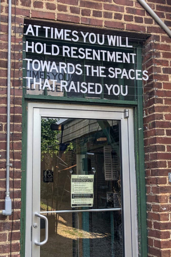white letters above a door to a brick building reads "at times you will hold resentment towards the spaces that raised you"