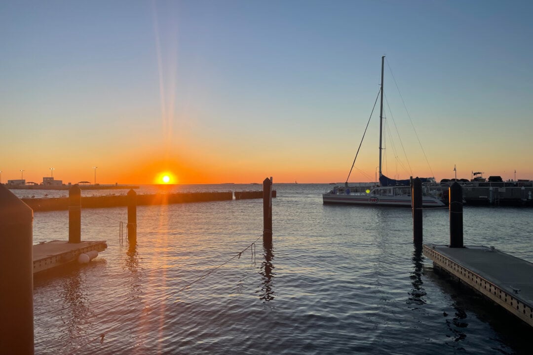 the sun sets on the horizon over water with sail boats and wooden piers