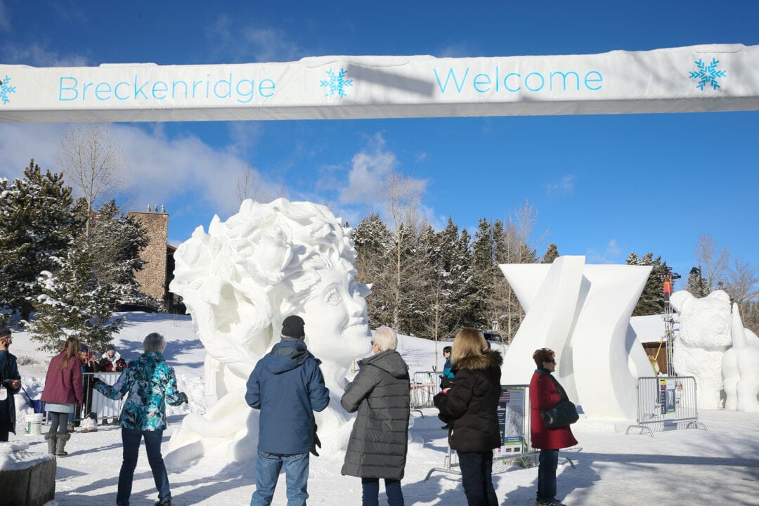 people gather outside under a banner that says breckenridge welcome and look at carved snow sculptures