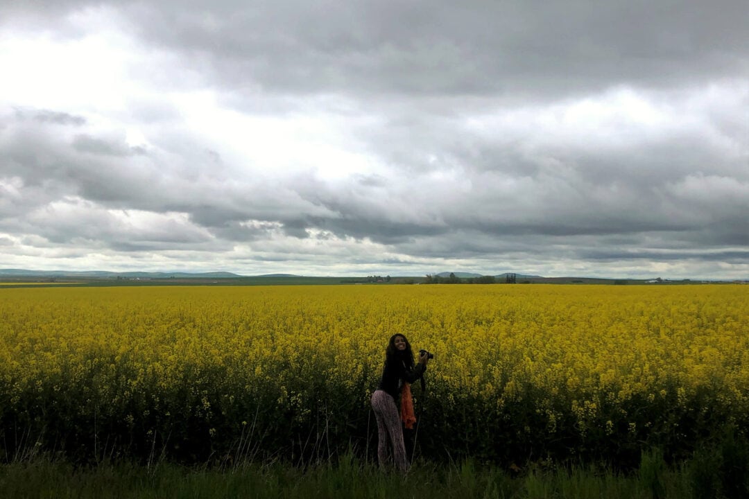a woman stands in a field of yellow flowers smiling under a grey cloudy sky