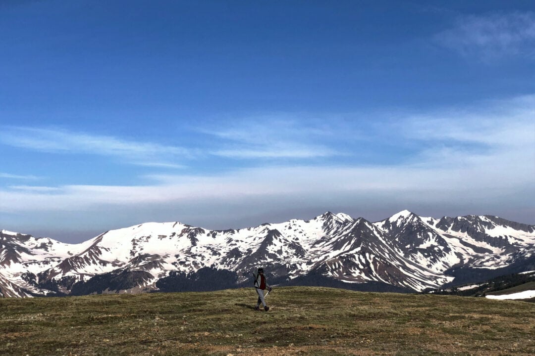 a person walks with snow capped mountains in the background under blue skies