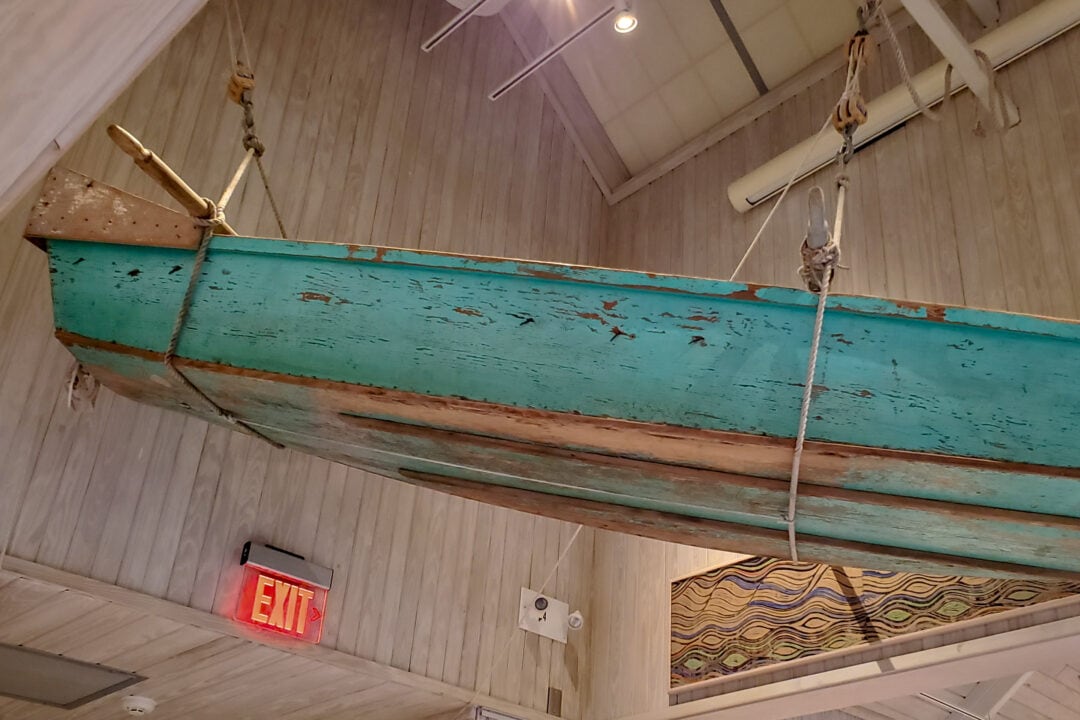 a bright blue wooden skiff boat hangs in a museum