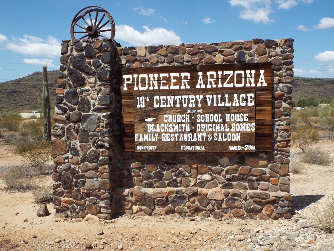 a wood and stone sign in the desert that says "Pioneer Arizona 19th century village"