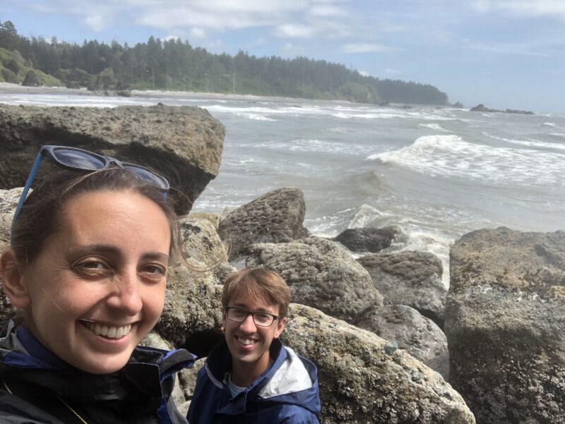 Two people at Ruby Beach next to big rocks and rough waters in the background.