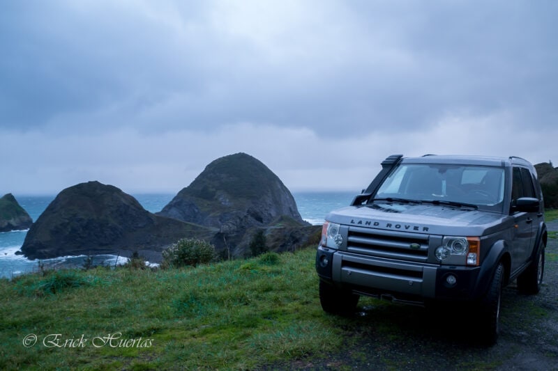 a silver land rover sits near the water under dark skies and green grass