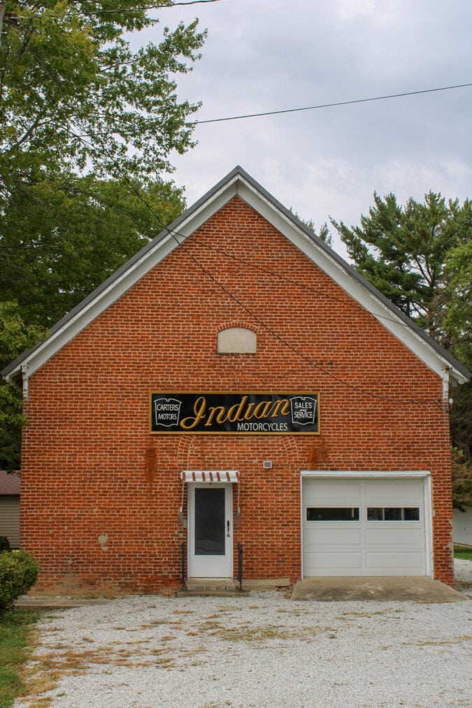 a brick building with a pointed roof and white trim has a sign advertising indian motorcycles