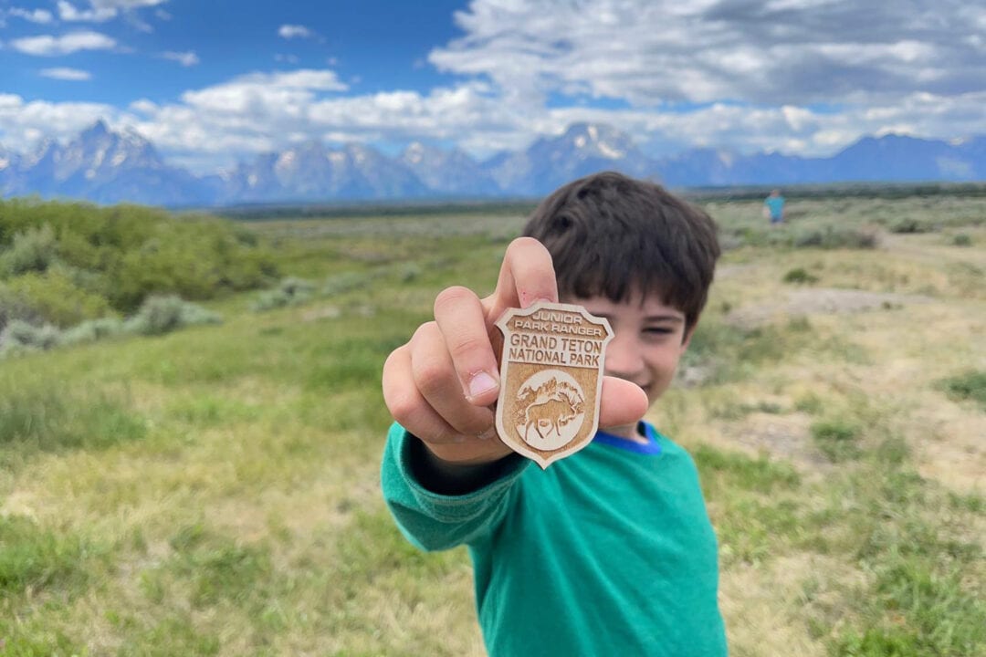 a boy holds a junior ranger badge outside