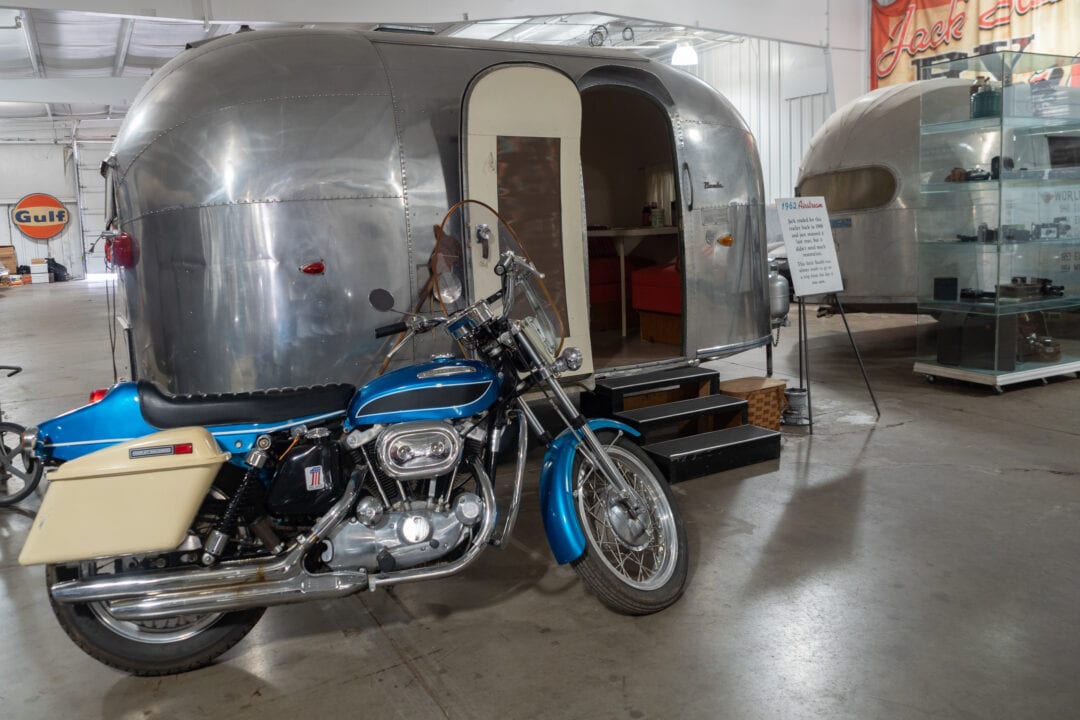 A vintage silver airstream trailer and blue motorcycle on display in a museum
