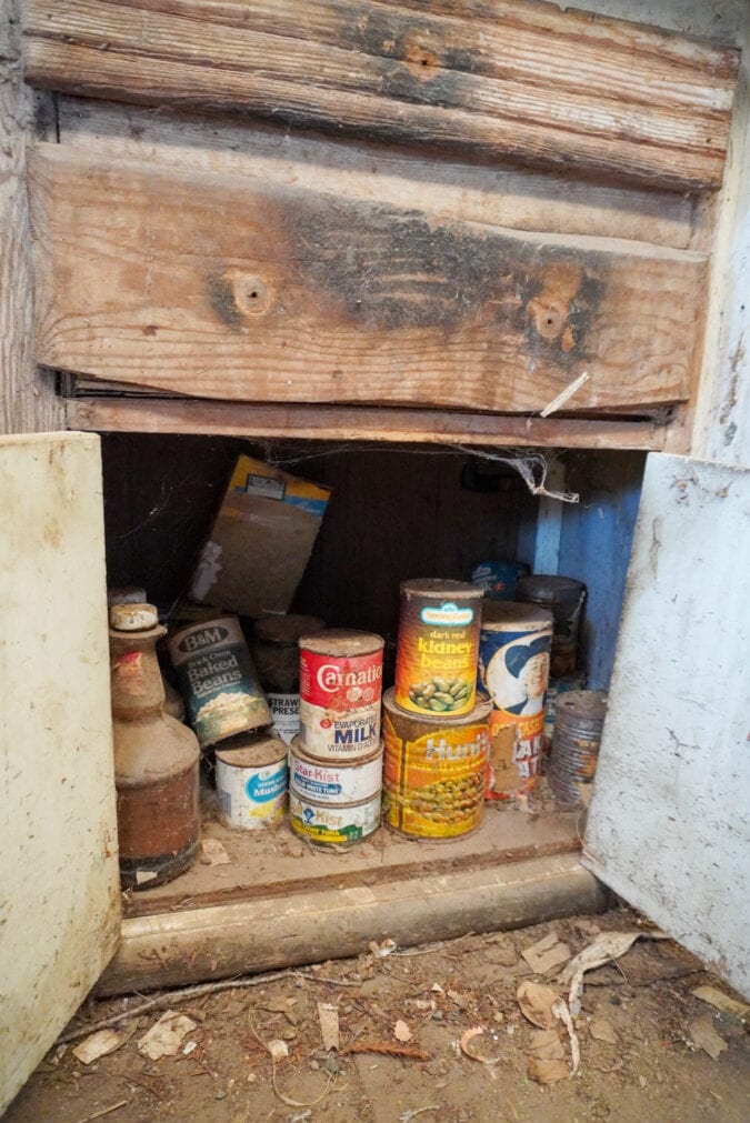 A dusty stack of canned food in an open kitchen cabinet